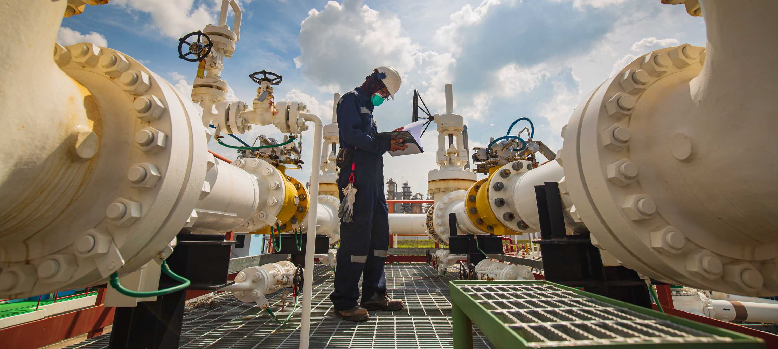 A picture of an man inspecting some industrial pipe and valves at a plant