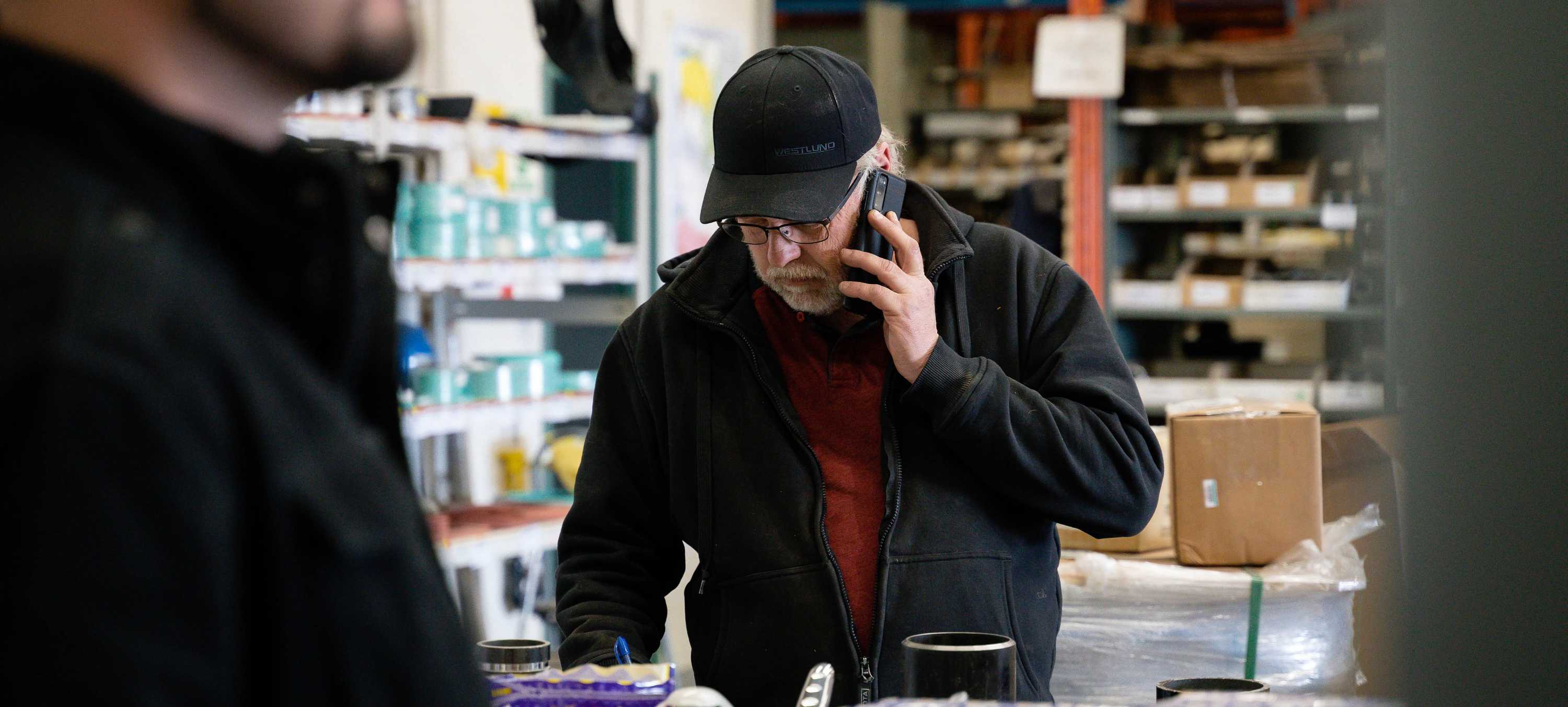A Picture of a man on a cell phone taking notes down in a warehouse