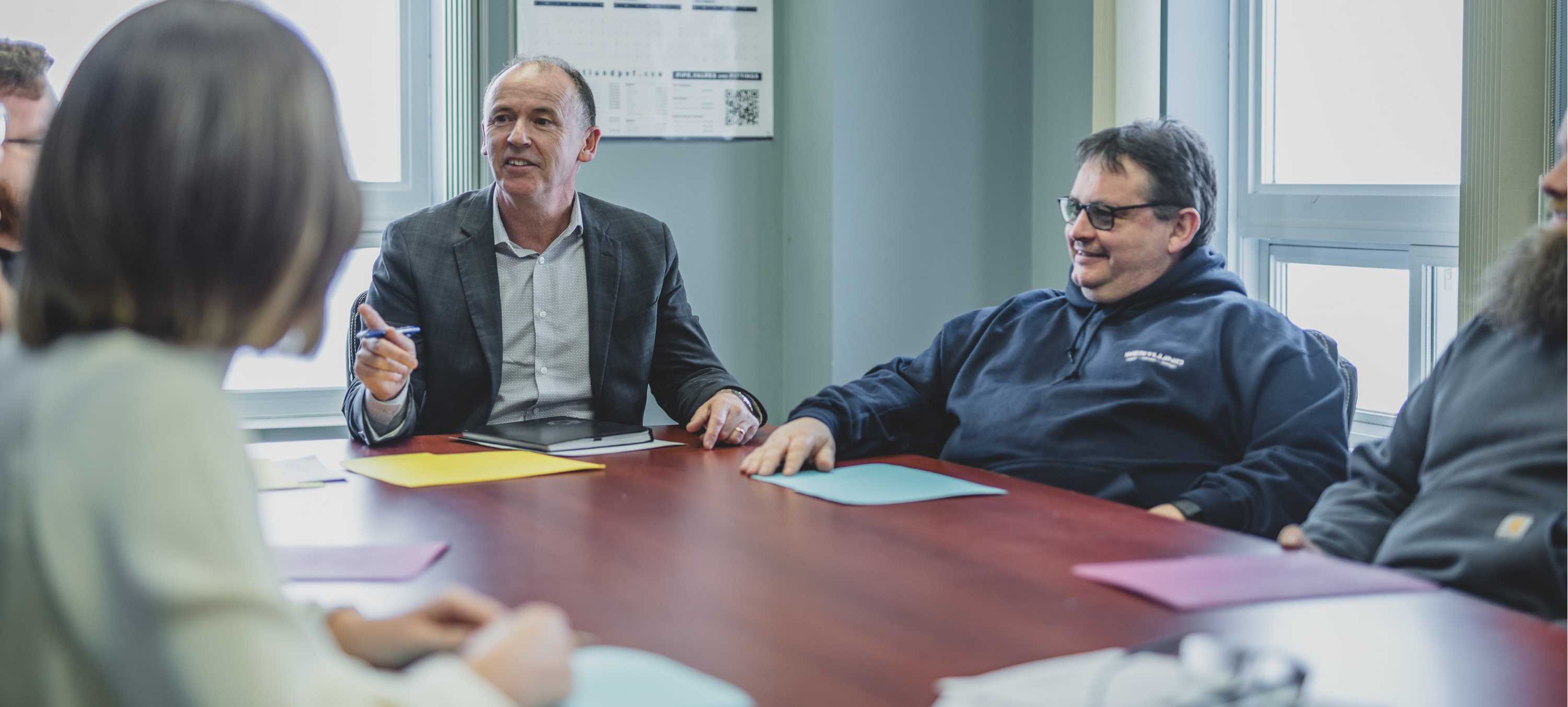 A Picture of people sitting around a board table having a meeting.